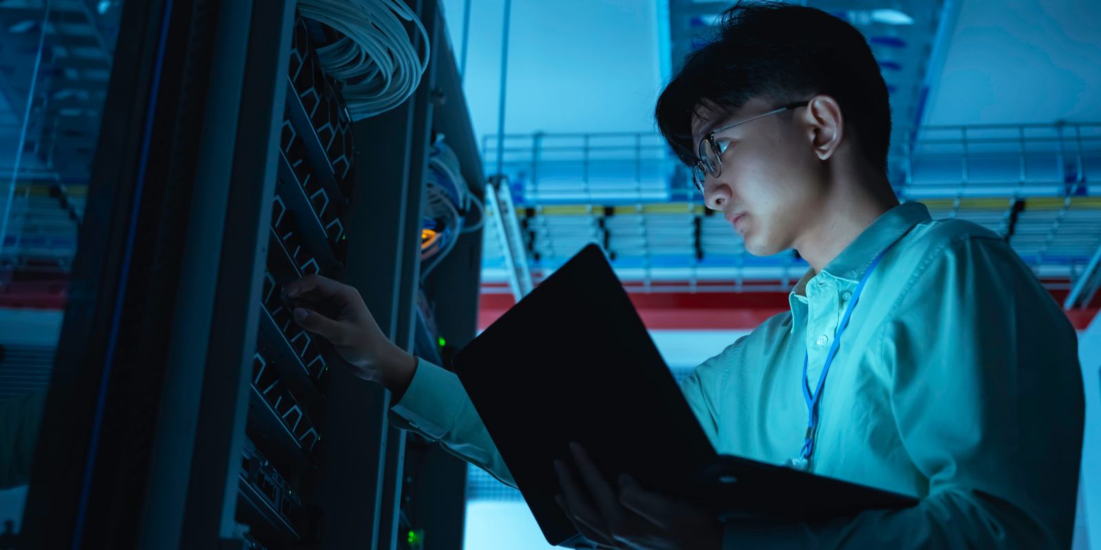 A cybersecurity engineer holding a laptop while inspecting server hardware in a data center representing hands-on cybersecurity preparedness