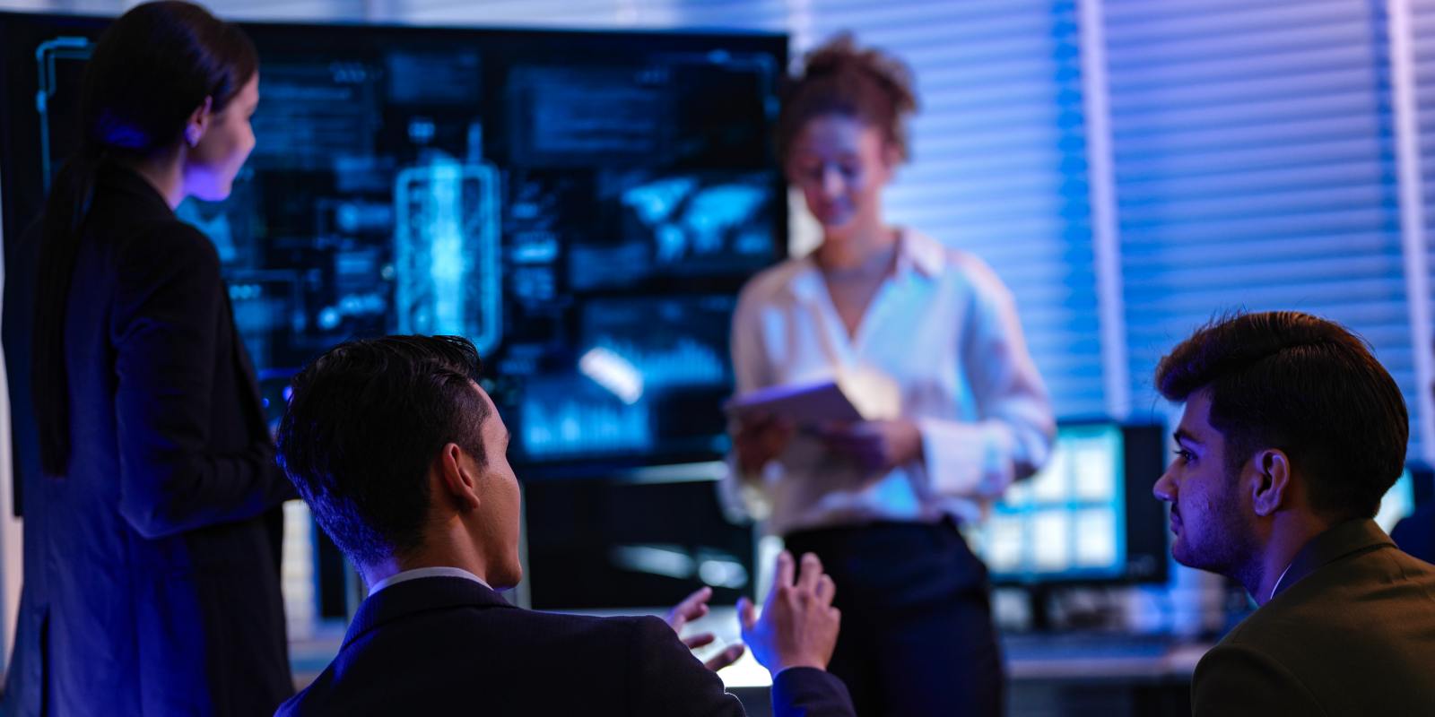 A team of cybersecurity professionals collaborating in a dark operations center with multiple monitoring screens representing a cybersecurity engineering team at work