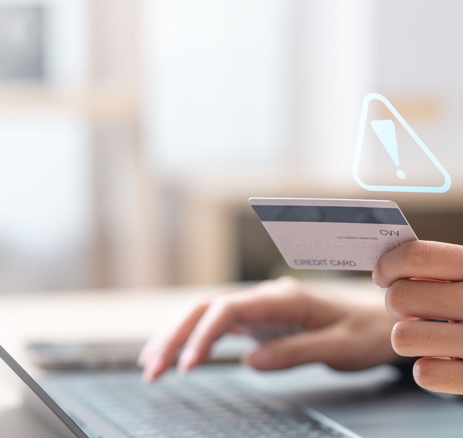 Person holding a credit card near a laptop with a security warning alert indicating financial data theft risk