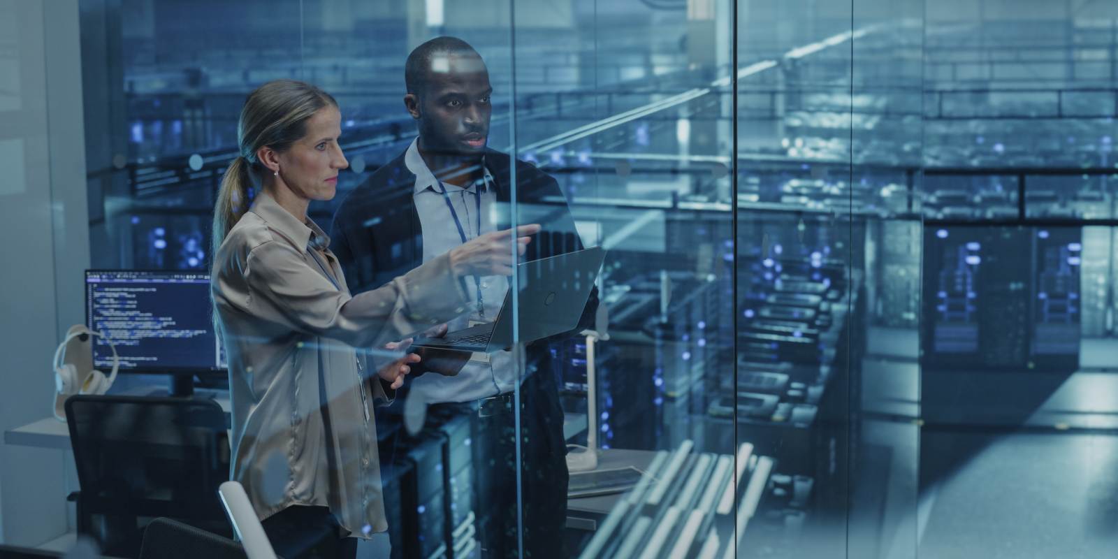 Two cybersecurity consultants collaborating with a laptop in front of a server room, representing expert IT security consultation