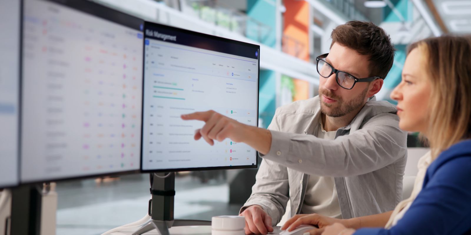 Two cybersecurity consultants reviewing a risk management dashboard on a large monitor, representing collaborative cybersecurity assessment and consulting