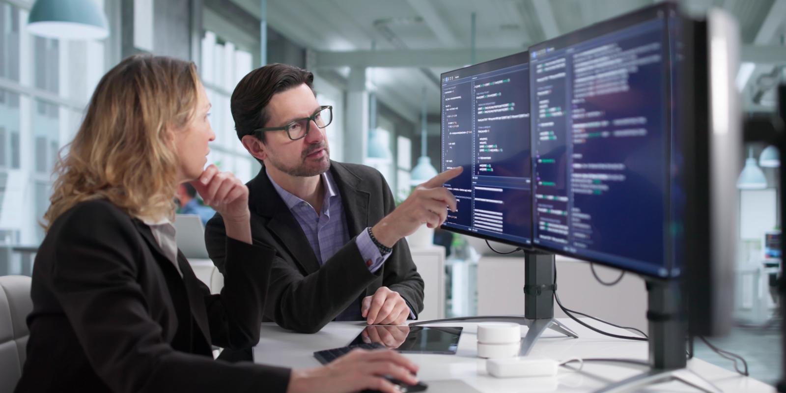 Two cybersecurity professionals reviewing and discussing code on dual monitors representing collaborative cybersecurity training