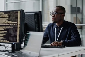 african american young developer in eyeglasses concentrating on his online work on computer sitting at workplace